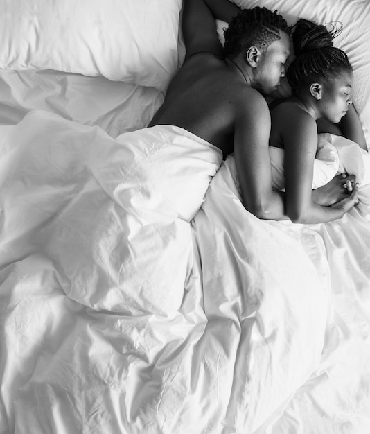 Foto preto e branco de casal de ascendência africana dormindo na cama, aconchegando-se e abraçando