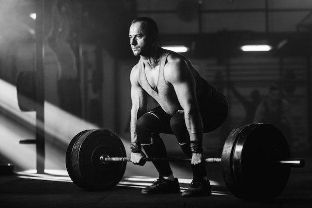 Foto preto e branco de homem de construção muscular realizando levantamento terra no treinamento esportivo em uma academia