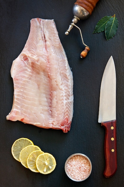 La foto del primer del filete de pescados crudos fresco con la sal y el limón del mar en fondo concreted negro de la tabla.