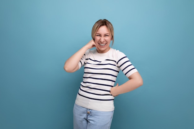 Foto de primer plano de una adorable y alegre chica rubia feliz con un suéter casual a rayas en un azul