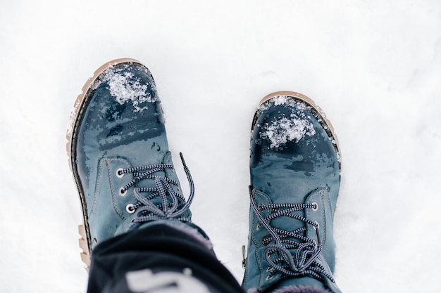 Foto de primer plano de botas cálidas azules de invierno con cordones en la nieve haciendo huellas en el suelo cubierto de nieve Asombroso fondo lleno de blanco y espectáculo