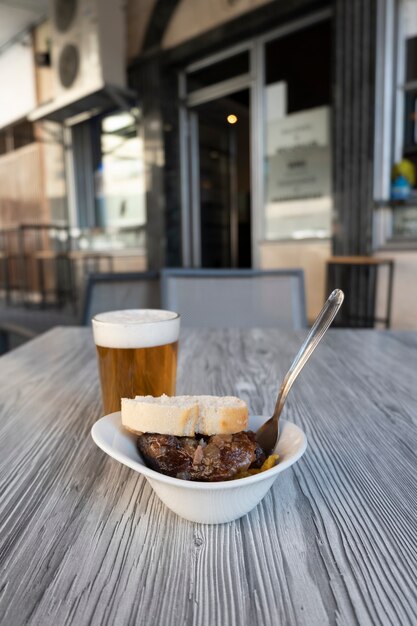 Foto en primer plano de una cerveza fresca en un vaso y un aperitivo de carrilleras de cerdo en la terraza de un bar español