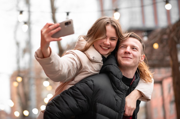 Foto de primer plano de una chica y su novio divirtiéndose juntos, mientras la chica monta sobre su espalda y se toma una selfie