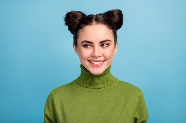 Foto de primer plano de una dama bastante divertida adolescente dos bollos graciosos lindos buen humor mirada engañosa lado espacio vacío usar suéter de cuello alto verde cálido aislado pared de color azul