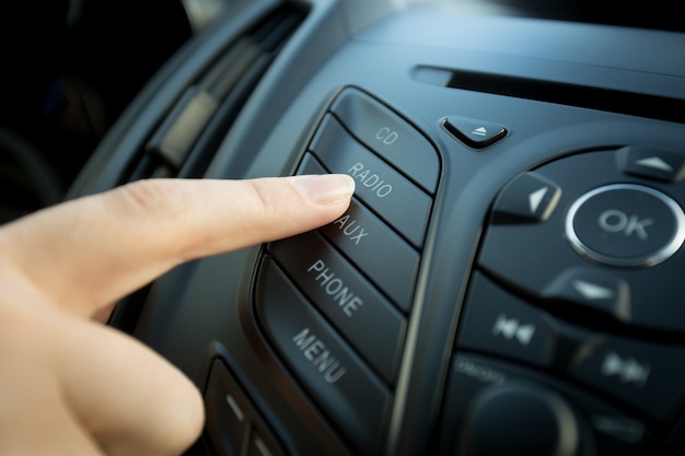 Foto en primer plano del dedo femenino presionando el botón de radio en el panel de control del automóvil