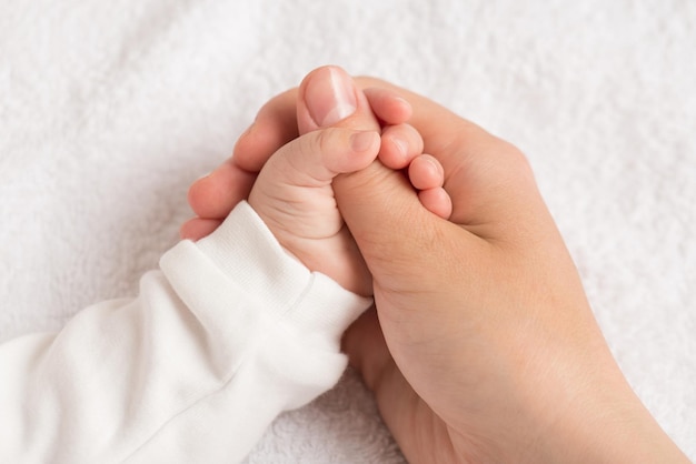 Foto de primer plano de la diminuta mano del recién nacido apretando el pulgar de la madre sobre un fondo textil blanco aislado