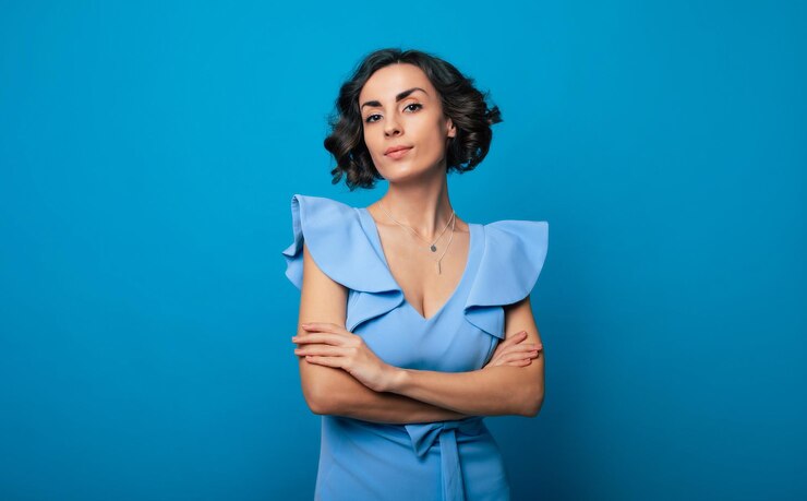 Foto foto de primer plano de una encantadora mujer sana con un vestido azul, que mira a la cámara y sonríe, mientras está de pie y posa aislada en el fondo azul