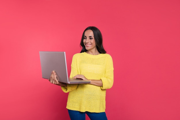 Foto de primer plano de una hermosa gerente con ropa informal, que sostiene una computadora portátil en su mano derecha y lee algo en la pantalla mientras sonríe ampliamente.