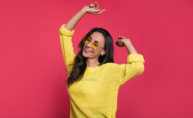 Foto de primer plano de una hermosa joven con un traje amarillo y gafas de sol, que se ríe con los ojos cerrados y posando