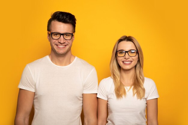 Foto de primer plano de un hombre y una mujer, posando delante de camisetas blancas y gafas y sonriendo mientras mira a la cámara