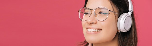 Foto de primer plano de una joven encantadora con gafas y escuchando música con auriculares inalámbricos blancos