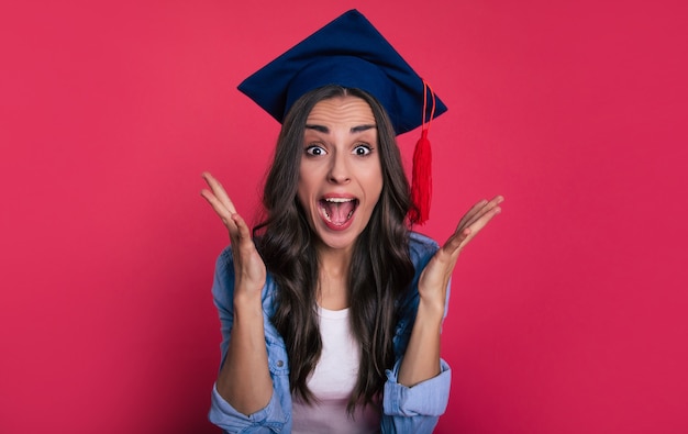 Foto foto de primer plano de una linda estudiante con una blusa y un sombrero académico cuadrado, que está muy contenta y grita de felicidad por su éxito
