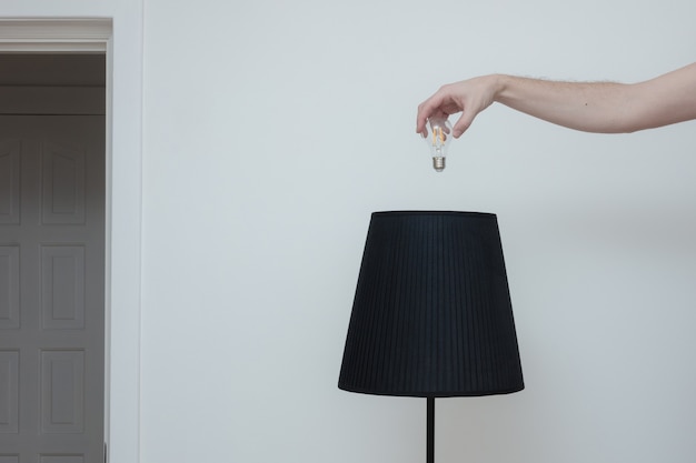 Foto de primer plano de una mano cambia una bombilla en una elegante lámpara de loft desde el lado superior y el interruptor de luz en la habitación cerca de la salida del apartamento