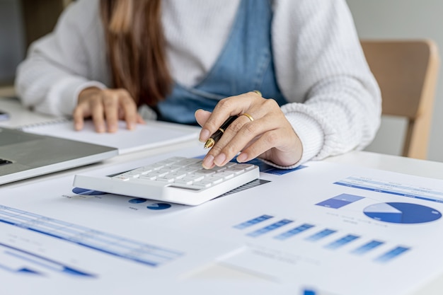 Foto de primer plano La mano de una mujer está presionando una calculadora, ella usa la calculadora para calcular los documentos para verificar la exactitud antes de traer el resumen de la reunión. Conceptos financieros.