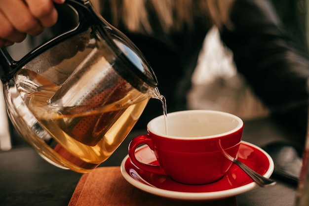 Foto de primer plano de la mano de la mujer vertiendo té de la tetera en una taza