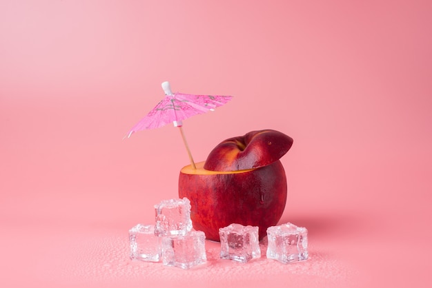 Foto de primer plano de manzana cortada con un paraguas de cóctel y derritiendo cubitos de hielo aislado sobre fondo rosa con copyspace