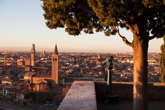 Una foto en primer plano de un monocular público en la cima de una montaña con espectaculares vistas aéreas de la antigua ciudad de Verona en Italia amanecer dorado de la mañana