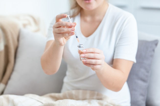 Foto en primer plano de una mujer acostada en la cama y llenando la jeringa con medicamentos