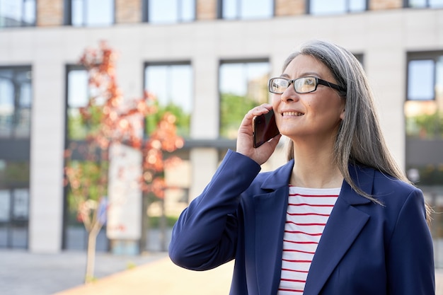 Foto de primer plano de una mujer canosa positiva con gafas tener una conversación telefónica