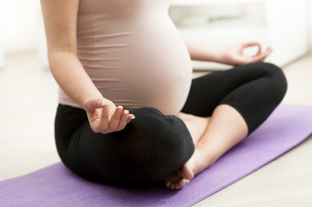 Foto en primer plano de la mujer embarazada sentada en posición de loto de yoga en el piso