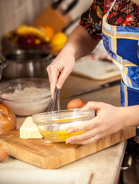 Foto en primer plano de mujer mezclando huevos en un tazón de vidrio.