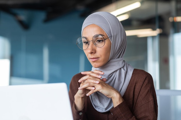 Foto de primer plano de una mujer de negocios satisfecha mirando la pantalla de un portátil mujer musulmana en hijab trabajando