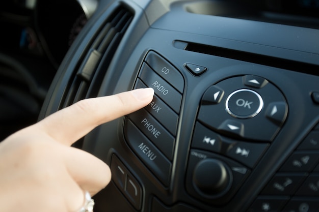 Foto en primer plano de la mujer presionando el botón de radio en el salpicadero del coche