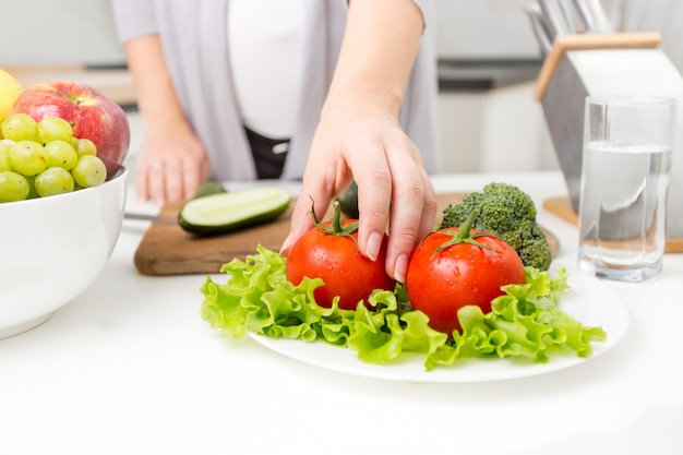 Foto en primer plano de una mujer recogiendo tomate fresco de la mesa en la cocina