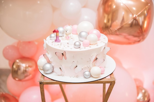 Foto de primer plano de un pastel de cumpleaños para 1 año Postre rosa cremoso con número de mariposas y decoración de bolas