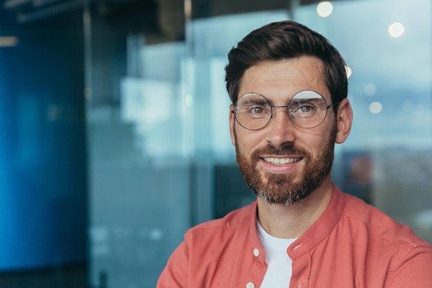 Foto de primer plano de un programador sonriente feliz y exitoso en un hombre de camisa casual roja con gafas mirando