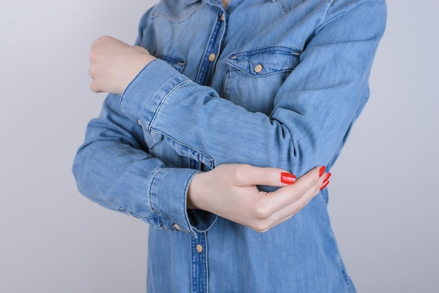 Foto de primer plano recortada de infeliz sufriendo de dolor dama tocando el codo aislado en el espacio de copia de fondo gris vistiendo ropa casual de jeans de mezclilla