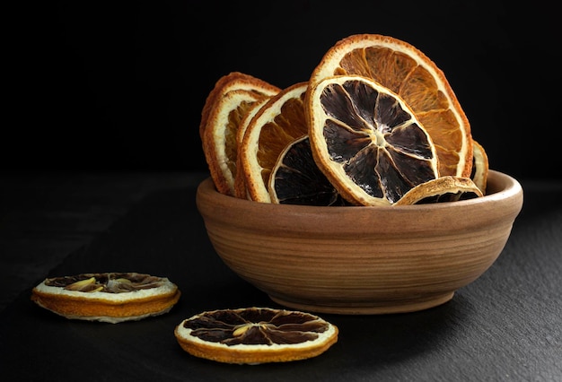 Una foto en primer plano de rodajas secas de limón y naranja en una taza sobre una superficie oscura