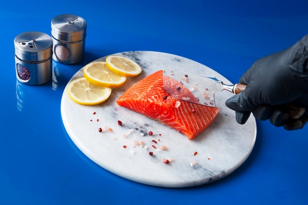 Foto de primer plano de salmón crudo fresco, filete de trucha en la tabla de cortar de mármol con rodajas de sal, pimienta y limón