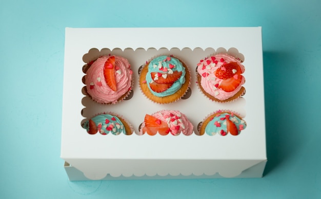 Foto en primer plano de seis coloridos cupcakes decorados con chispas y fresas en caja de papel cerrada