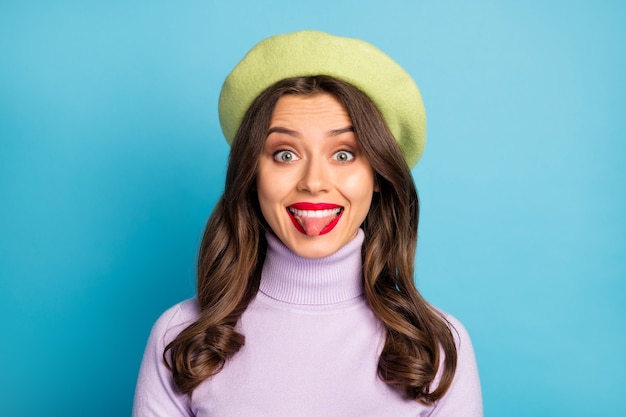 Foto en primer plano de la señora bonita sacando la lengua boca buen humor labios rojos persona infantil usar boina verde sombrero cuello tortuga púrpura aislado pared de color azul