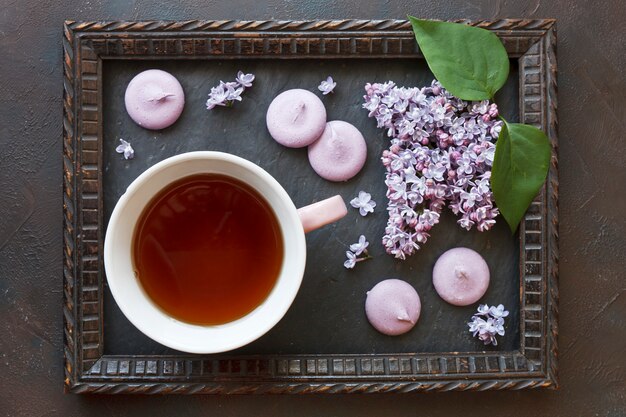 Foto de primer plano de la taza de té con macarrones y lila fresca hermosa en el marco en mesa negro