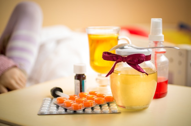 Foto en primer plano de té, tarro de miel y pastillas sobre la mesa en el dormitorio