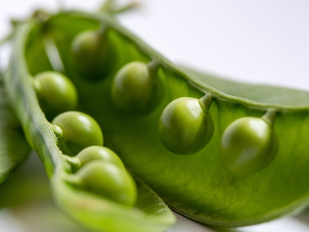 Foto en primer plano de una vaina abierta de guisantes y guisantes en el interior sobre un fondo blanco.