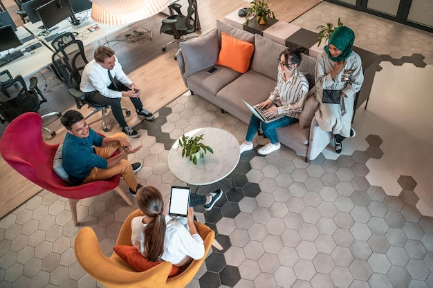 Foto foto de primera vista del equipo de negocios multiétnico que tiene una lluvia de ideas en el área de relajación del interior de la oficina moderna que trabaja en una computadora portátil y una tableta. foto de alta calidad