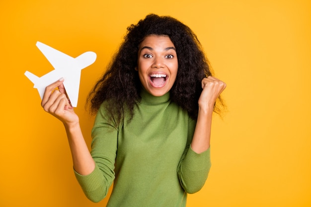 Foto de raza mixta positiva linda chica muy hermosa ganó boletos para ir al extranjero en avión regocijándose emociones emocionadas sosteniendo plano aislado fondo de color amarillo vivo ondulado rizado