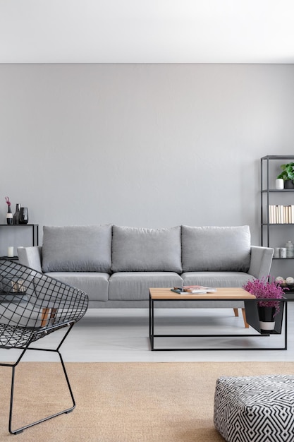 Foto real del interior de una sala de estar simple con un sofá gris, sillón, mesa de centro y alfombra marrón Pared vacía, coloque su gráfico