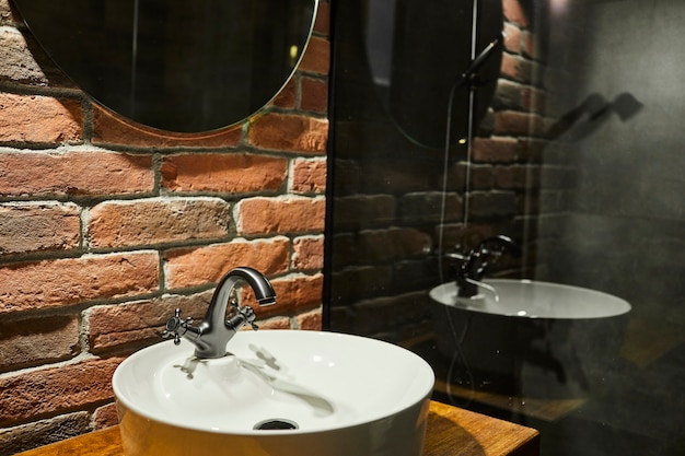 Foto real de un lavabo en el interior de un baño con pared de ladrillo y espejo