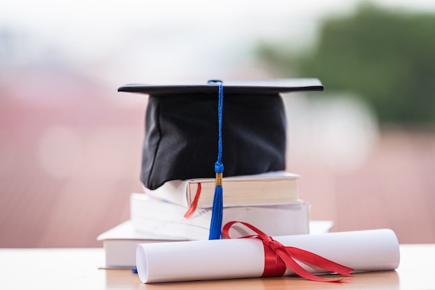 Foto recortada de un birrete de sombrero de graduación universitaria y certificado de diploma en la mesa