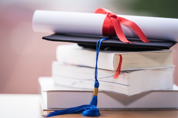 Foto recortada de un birrete de sombrero de graduación universitaria y certificado de diploma en la mesa