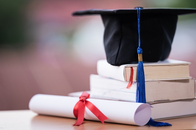 Foto recortada de un birrete de sombrero de graduación universitaria y certificado de diploma en la mesa