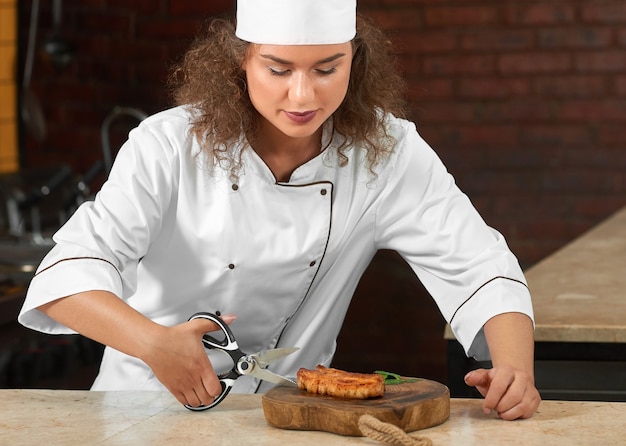 Foto recortada de una chef profesional cortando carne a la parrilla con unas tijeras mientras trabajaba en la cocina del restaurante.