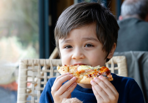 Foto recortada Chico lindo niño comiendo pizza casera en el café