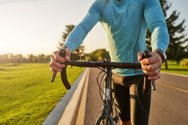 Foto recortada de ciclista atlético en ropa deportiva caminando con su bicicleta después de entrenar en