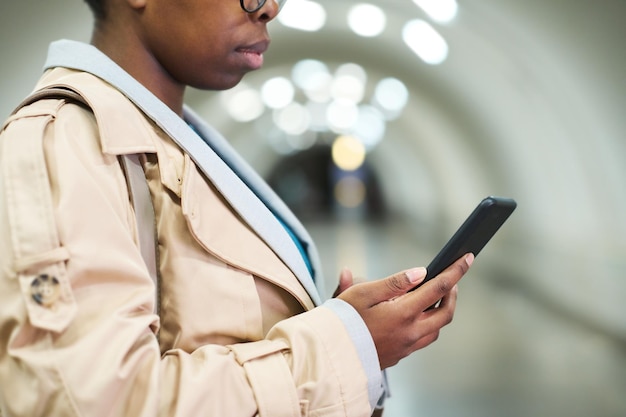 Foto recortada da vista lateral da mulher negra em sobretudo bege segurando smartphone
