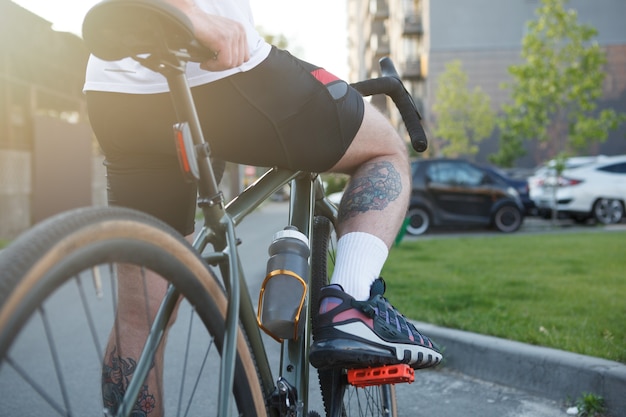 Foto recortada da vista traseira de um ciclista tatuado em sua bicicleta